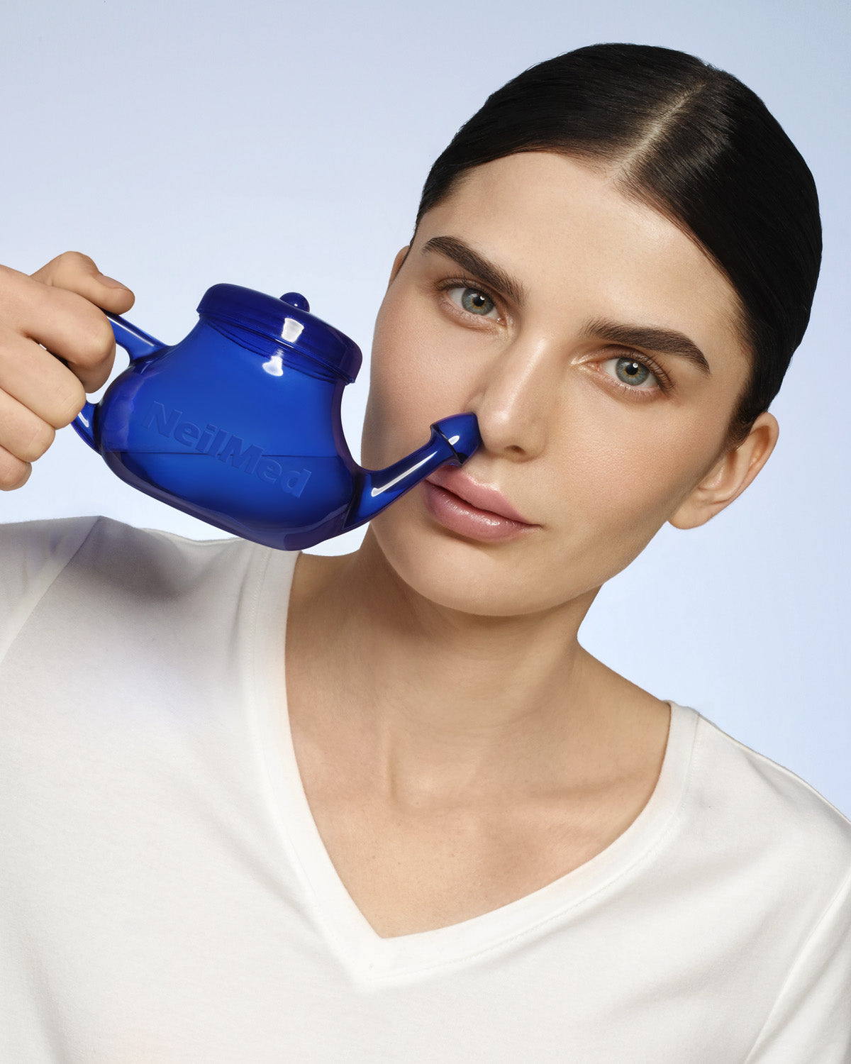 Person using a blue neti pot against a light gray background