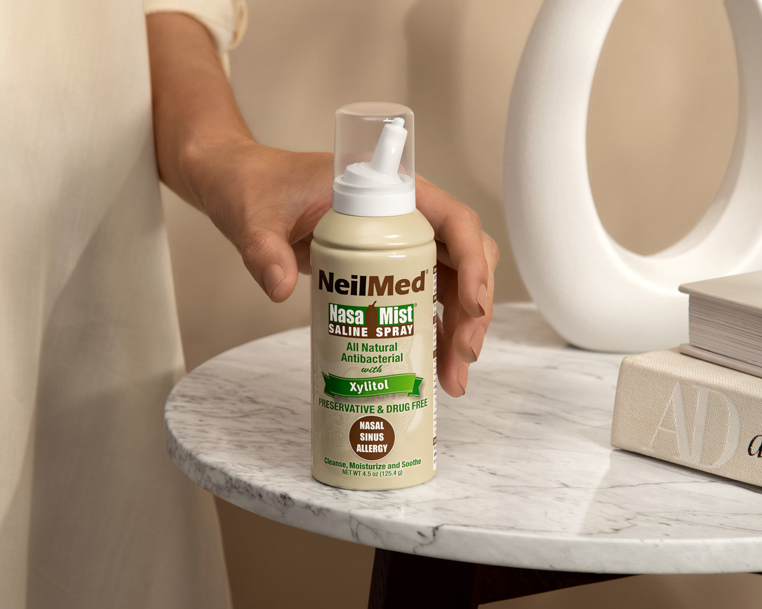 Hand holding a bottle of NeilMed NasaMist saline spray on a marble surface.