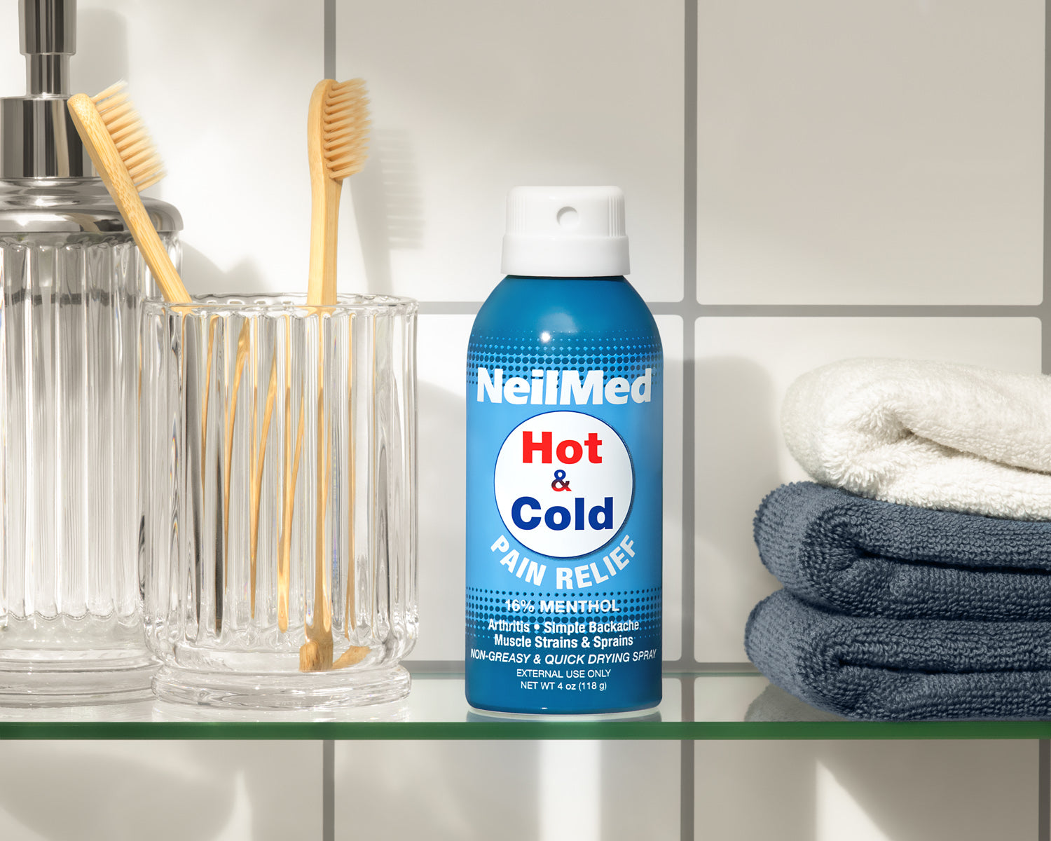 NeilMed Hot & Cold Pain Relief spray bottle on a bathroom shelf with toothbrushes and towels.