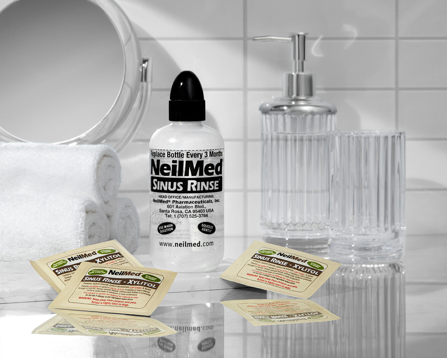 NeilMed Sinus Rinse Xylitol packets with bottle on bathroom counter with mirror and white towels in the background