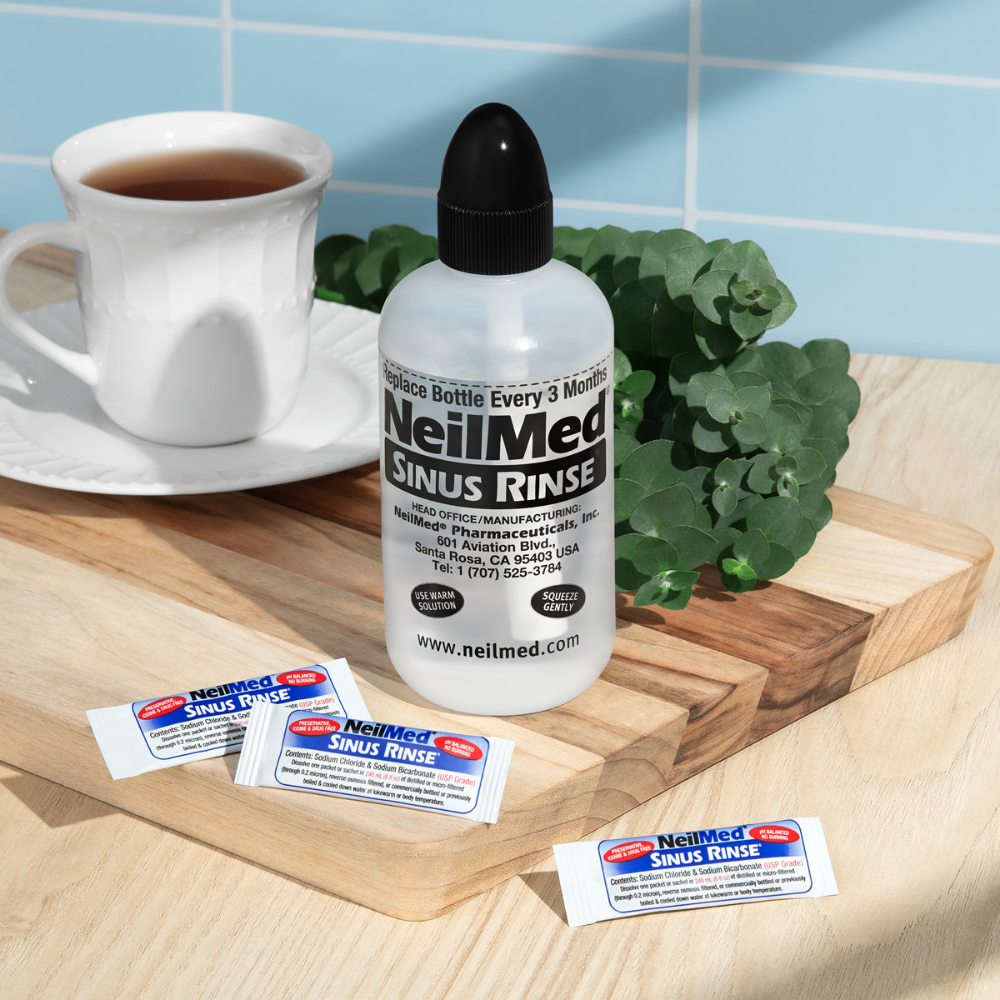 NeilMed Sinus Rinse bottle with packets on a wooden tray with a cup of tea and plant in the background.